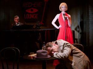 One chanteuse after another (Sharon Rietkirk) runs over hapless Sam Galahad (Kevin Bailey, seated and passed out) as a nonplussed Buddy Toupee (Jeffrey Rockwell) looks on. Photos by Aaron Rumley.